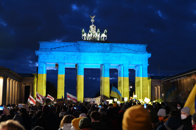 Eine Menschenmenge steht vor dem Brandenburger Tor in Berlin und hält Fahnen und Plakate, mit einer Banner auf der rechten Seite des Bildes.