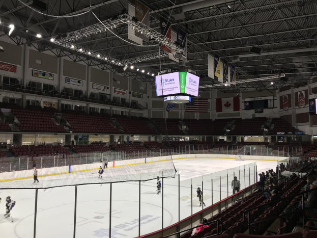 Ein Eishockeyspiel in einer großen Arena mit einem zentralen Netz, Zuschauern auf beiden Seiten, Deckenbeleuchtung und Bannern sowie der St. Louis Blues Arena-Branding.