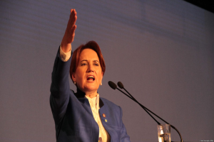 Eine Frau steht an einem Podium mit zwei Mikrofonen und einem Glas Wasser, spricht vor einem Bildschirm und scheint eine Regierungsentscheidung zur Abschaffung der Frauenrechte anzusprechen.