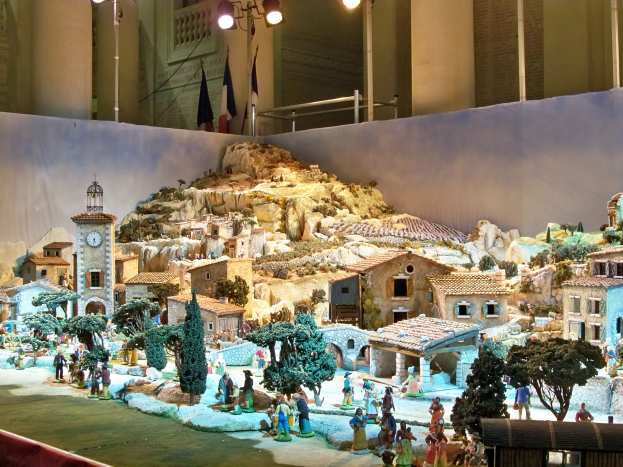 Ein detailliertes Miniatur-Modell einer Krippe des Weihnachtsfestes in einem Museum ausgestellt, mit Figuren, Gebäuden, Bäumen und Beleuchtungselementen, beleuchtet von der Museumsbeleuchtung.