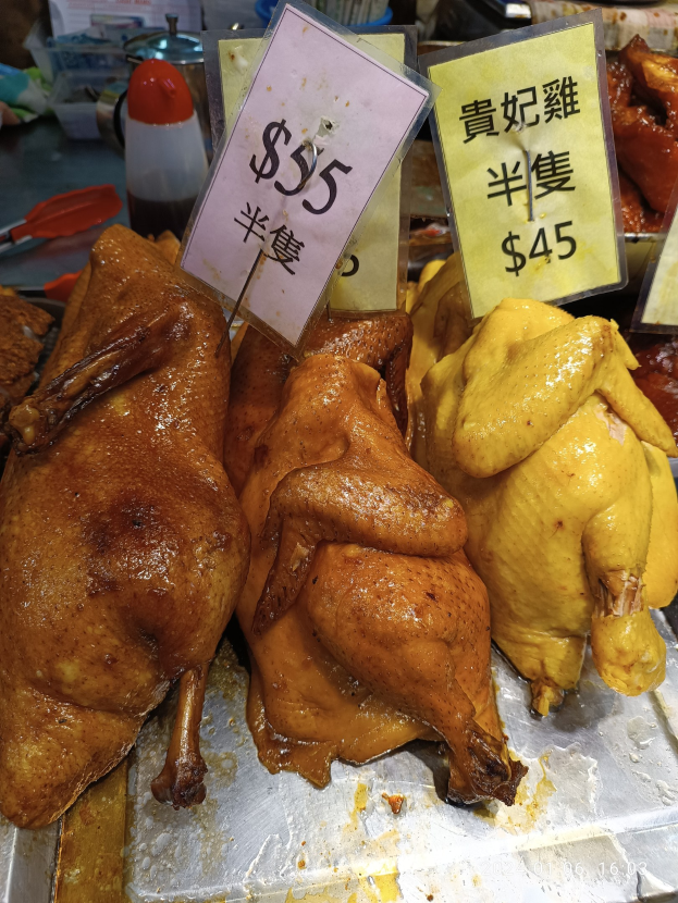 Hühner auf einem Metalltablett mit Preisschildern in einem belebten Markt.