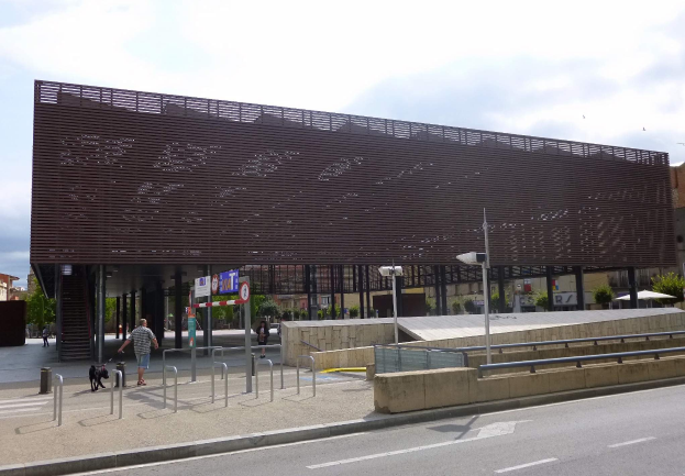 Großes modernes Gebäude mit zahlreichen Fenstern, das den neuen Eingang zur Stadtmitte bildet und von Straßeninfrastruktur und urbaner Aktivität flankiert wird.