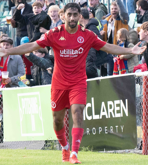 Ein Fußballspieler in roter Uniform rennt auf einem Feld mit ausgestreckten Armen, umgeben von Zuschauern hinter einem Zaun, mit einem "Middlesbrough FC v Swansea City - Sky Bet Championship"-Schild im Hintergrund.
