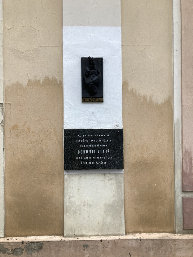 Schwarze Tafel an einem Gebäude mit einer darauf liegenden Hand, mit Inschrift zur Erinnerung an Holocaust-Opfer.