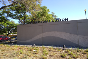 Außenansicht des Houston Holocaust Museums mit eingravierter Textwand, Gedenksteine, Landschaft, Straßenverkehr, Straßenlaterne und bewölktem Himmel.