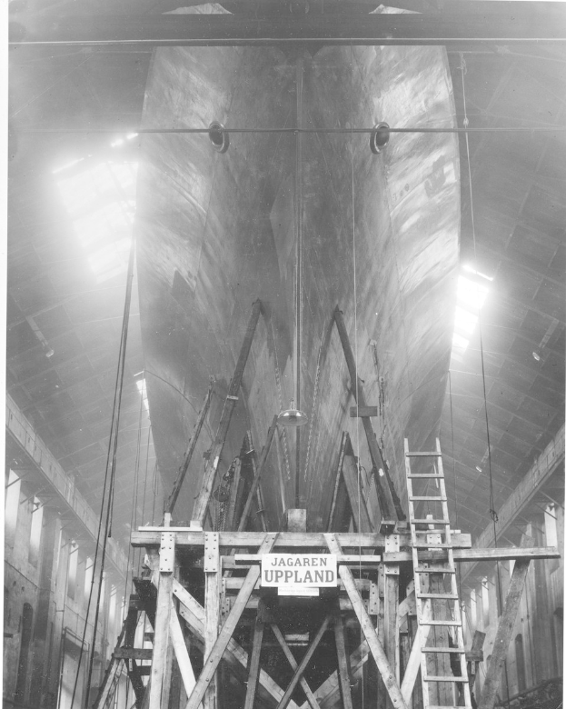 Großes schwarzes und weißes Schiff in einem Schiffbauwerk mit Stützkonstruktionen, einer Leiter, einem Schild, einer Deckenbeleuchtung und Fenstern.
