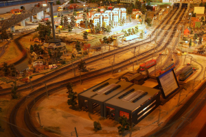 Eine detaillierte Miniatur-Modellbahnanlage in einem Museum, die Gebäude, Bäume, Eisenbahnschienen, Fahrzeuge, Pfosten, Lichter und Schilder enthält und eine belebte Stadtlandschaft nachahmt.