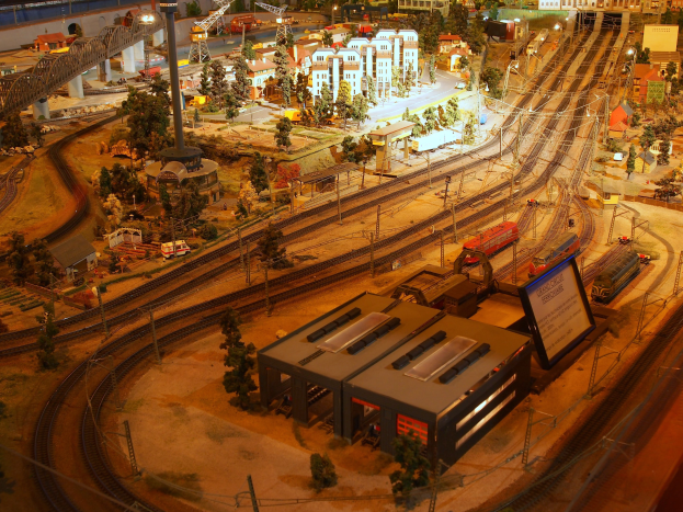 Eine detaillierte Miniatur-Modellbahnanlage in einem Museum, die Gebäude, Bäume, Eisenbahnschienen, Fahrzeuge, Pfosten, Lichter und Schilder enthält und eine belebte Stadtlandschaft nachahmt.