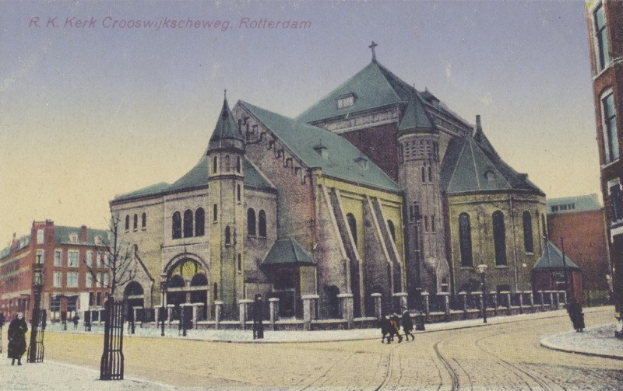 Altes Foto einer Kirche in städtischer Umgebung, umgeben von Gebäuden, Straßeninfrastruktur, Fahrzeugen, Fußgängern, Bäumen und einem klaren Himmel mit Text oben.