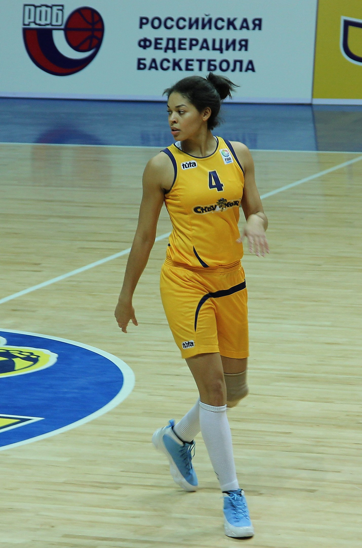 Ein professioneller Basketballspieler in einem gelben Trikot dribbelt auf einem Feld mit einer Tafel im Hintergrund.