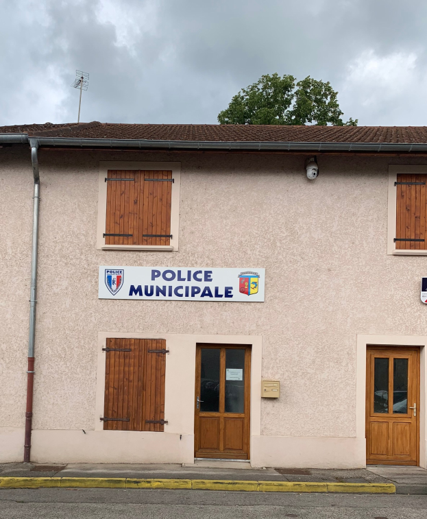 Gebäude der Polizei municipaux mit einem Schild, Fenstern, Türen, einer Namensschild, einem Rohr, einem Baum und einem bewölkten Himmel im Hintergrund.