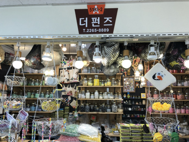 Ein unordentlicher Laden in Seoul mit verschiedenen Gegenständen wie Körben, Lampen, Flaschen und Spielzeugen auf Regalen, mit einem Schild oben, das ihn als einen der besten koreanischen Läden ausweist.