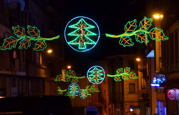 Eine nächtliche Stadtstraße, geschmückt mit festlichen Weihnachtslichtern mit Blättern und anderen Dekorationen, mit fahrenden Fahrzeugen und Gebäuden auf beiden Seiten.