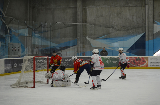 Gruppe von Menschen, die Eis-hockey auf einem Eisplatz mit Helmen und Hockey-Schlägern spielen, Torpfosten links, Banner und Wand im Hintergrund.