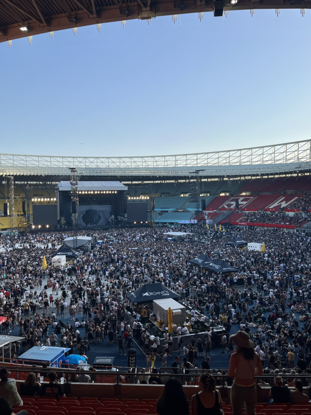 Große Menge sitzend und stehend in einem Stadion mit Zelten, Geländern und Überdachung, was auf ein Konzert in der O2 Arena in London hindeutet.