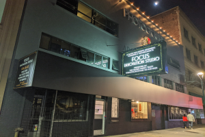 Außenansicht des Focus Innovation Studio in New York City bei Nacht, mit erleuchteten Fenstern, Namensschildern und Menschen, die auf dem Gehweg unter Straßenlaternen gehen.