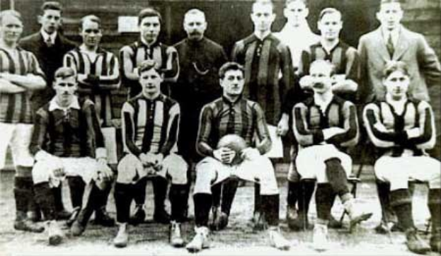 Schwarzes und weißes Foto von Mitgliedern der Fußballmannschaft von Ballymena Football Club, einige stehen und einige sitzen, vor einer Wand.
