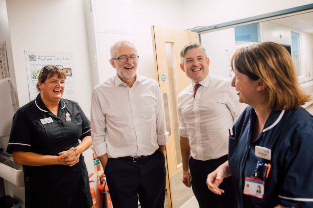 Vier Personen, die in einem Krankenhausflur lächeln und sich unterhalten, mit verschiedenen medizinischen Elementen im Hintergrund.