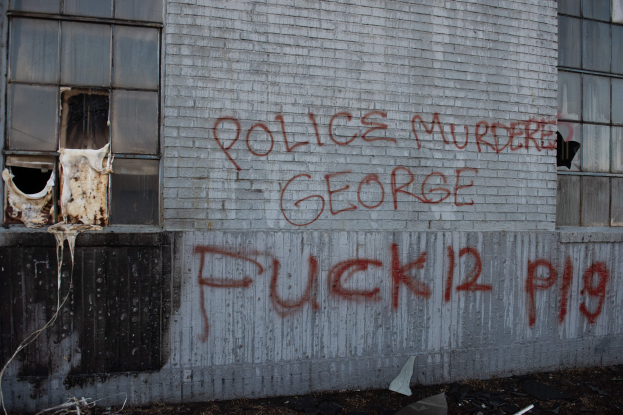 Ein Gebäude mit Graffiti, das "Polizei Mörder George Fuck 12 P19" auf der Seite trägt, mit Fenstern und verschiedenen Gegenständen davor.