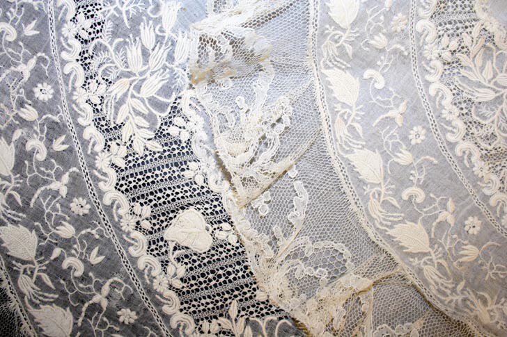 Nahaufnahme eines weißen Hochzeitskleids mit feiner Spitzenverzierung auf einem leichten, luftigen Stoff.