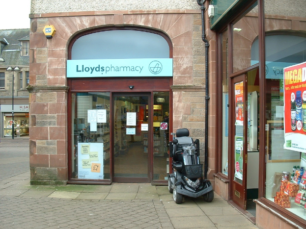 Eine Apotheke mit einem vor dem Gebäude geparkten Auto und einem Gebäude, das links sichtbar ist.