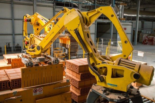 Großes industrielles Lagerhaus mit gestapelten Kisten, Überheadkranen, Zaun, Pfählen und einer fernen Wand in einer Fertigungsumgebung.