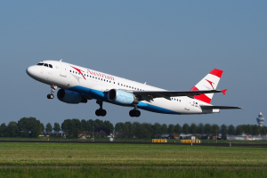 Airbus A320-200 der Austrian Airlines startet vom Frankfurter Flughafen mit grünem Gras darunter, Bäumen und Gebäuden im Hintergrund und einem Turm auf der rechten Seite.
