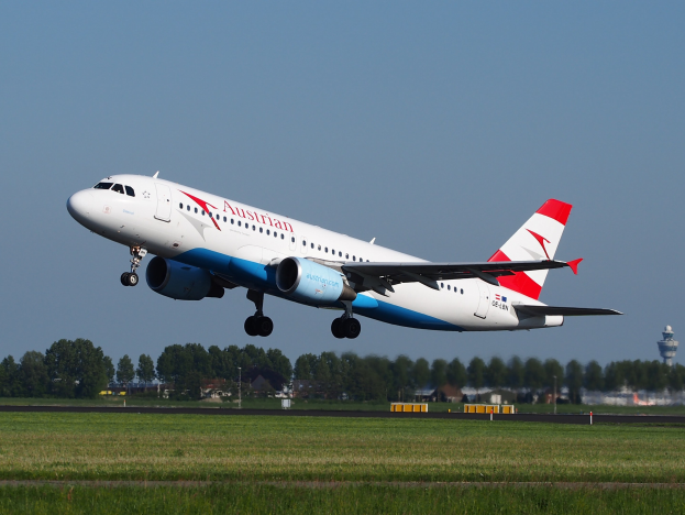 Airbus A320-200 der Austrian Airlines startet vom Frankfurter Flughafen mit grünem Gras darunter, Bäumen und Gebäuden im Hintergrund und einem Turm auf der rechten Seite.