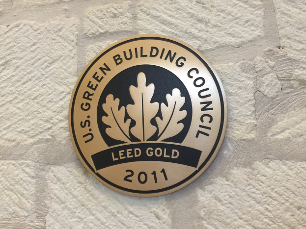 Logo der U.S. Green Building Council an einer Gebäudefassade, mit einem grünen Schild mit weißer Umrandung und schwarzer Schrift, umgeben von einem Lorbeerkranz.