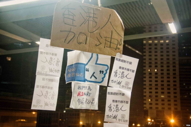 Eine Gruppe von Menschen vor einem beleuchteten Gebäude in der Nacht mit Protestschildern an der Decke.