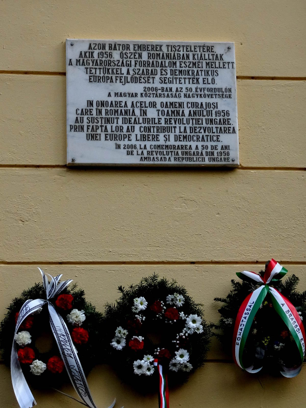 Zwei Kränze mit Bändern hängen an einer Gebäudefassade, dahinter eine Gedenktafel für Holocaust-Opfer.