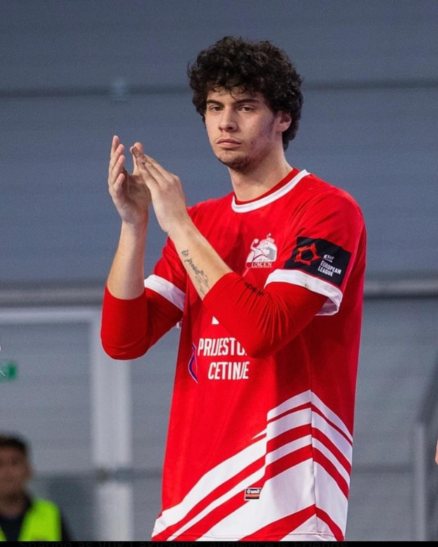Ein Mann in rot-weißem Shirt klatscht in der Vordergrund, im Hintergrund ist eine weitere Person und eine Wand zu sehen, Text unten lautet "Copenhagen Futsal Club - Foto 1".