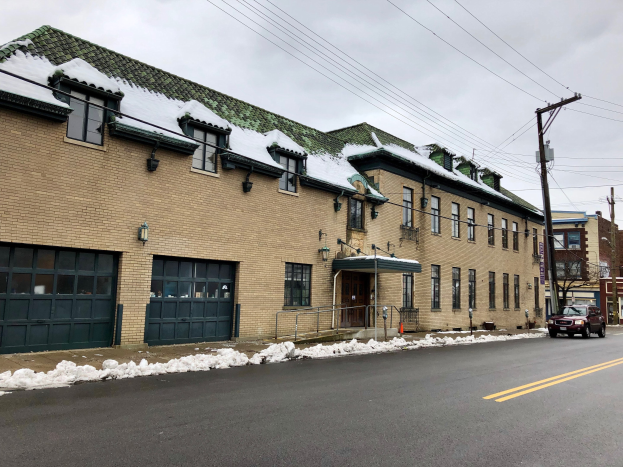 Großes Backsteingebäude mit grüner Dachfläche an einer Straßenkreuzung, als ehemalige St. Louis-Feuerwache bezeichnet, umgeben von Fahrzeugen, Schnee, Strommasten, Bäumen und einem bewölkten Himmel.