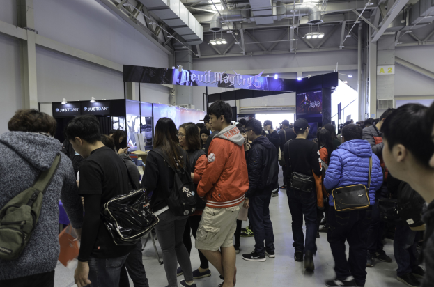 Gruppe von Menschen vor einer Menge an einer Gaming-Messe, mit Texttafeln, Deckenbeleuchtung und Rohren im Hintergrund.