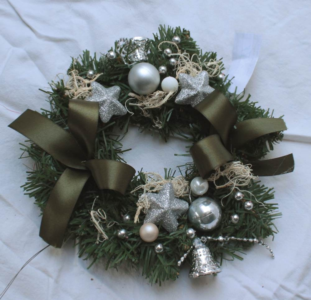 Ein festlicher Adventskranz mit Silberschmuck und Bändern auf einem weißen Tuch, mit bunten Kugeln, Sternen und anderen Verzierungen.