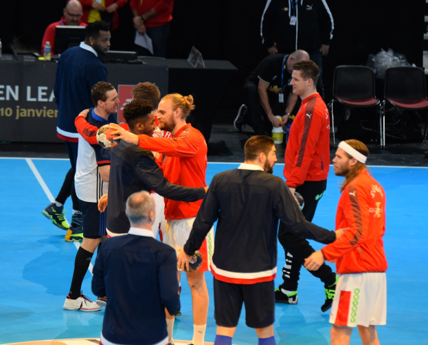 Mannengruppe auf einem Futsal-Platz mit Bällen, die mit Stühlen, einem Tisch mit Flaschen und Laptops sowie einer Tafel mit Text im Hintergrund feiern