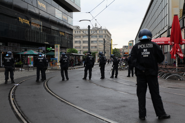 Gruppe von Polizeibeamten in schwarzen Uniformen und Helmen, die auf einer von Glasfenstern gesäumten Straße stehen.