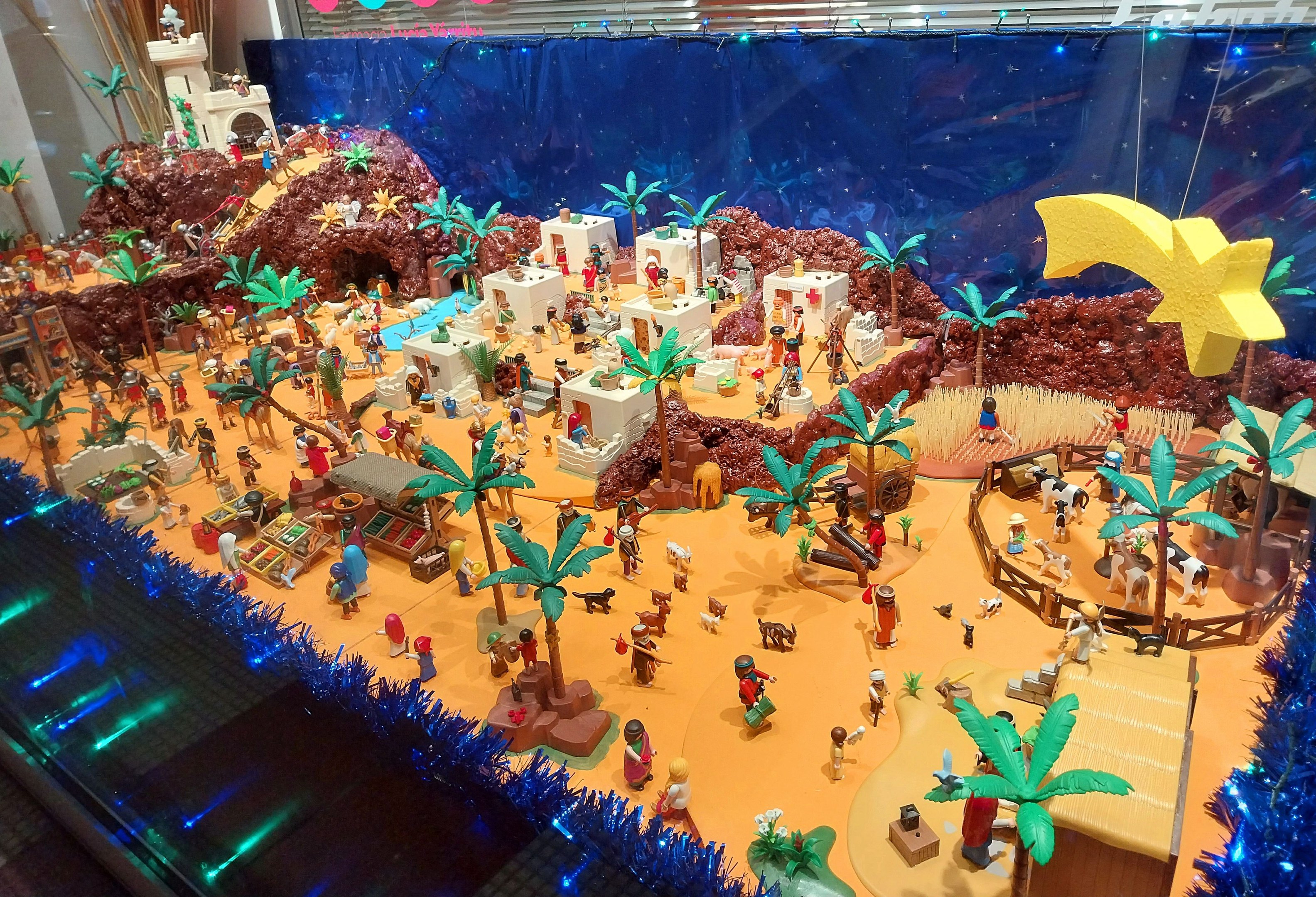 Vitrine voller verschiedener Lego-Steine und -Teile auf einem Tisch, umgeben von Spielzeugen, Bäumen und dekorativen Gegenständen, mit einer beleuchteten Wand im Hintergrund.