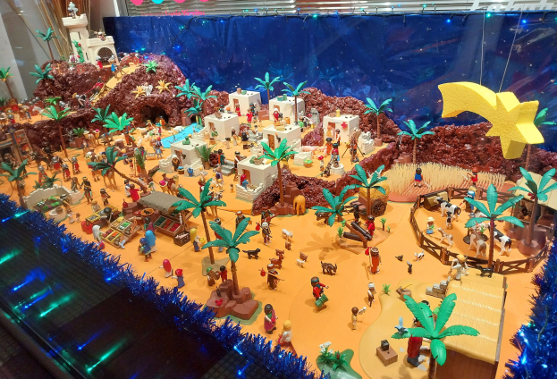 Vitrine voller verschiedener Lego-Steine und -Teile auf einem Tisch, umgeben von Spielzeugen, Bäumen und dekorativen Gegenständen, mit einer beleuchteten Wand im Hintergrund.