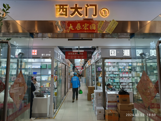 Innenseite einer chinesischen Apotheke mit Glaswänden, einer Pflanze links, Regalen mit Gegenständen, verstreuten Kartons und einem Namensschild oben.