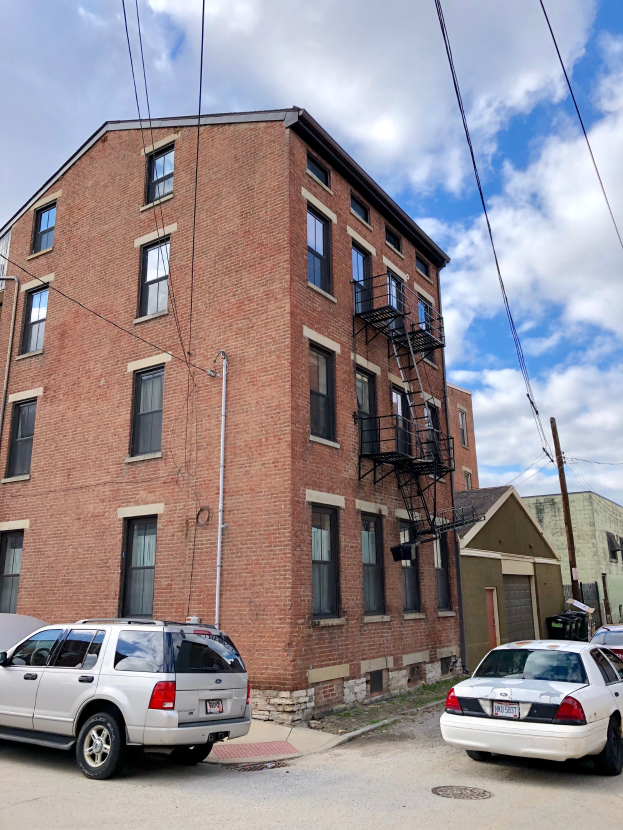 Ein Ziegelgebäude mit Fenstern, Treppen mit Geländern und parkenden Autos davor, mit einem Mast mit Drähten im Vordergrund und einem bewölkten Himmel im Hintergrund, mit Text unten, der die Vermietung von Wohnungen an 5901 S Elmwood Ave, Chicago 60618 anzeigt.