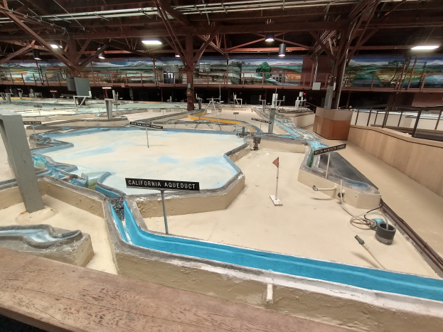 Ein großes Indoor-Wasserpark mit zahlreichen Wasserrutschen, Pfählen, Texttafeln, Deckenleuchten und Wandgemälden, das einem Minigolfplatz ähnelt.