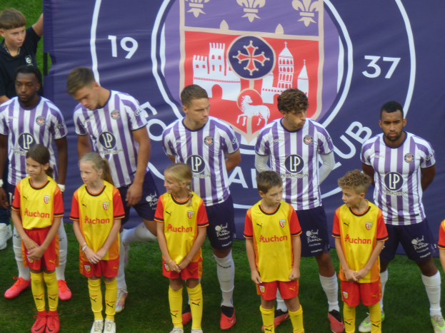 Eine Gruppe junger Menschen, die zusammen auf einem Fußballfeld stehen, mit einem Banner im Hintergrund, auf dem "Preston Primary School Football Team" steht.