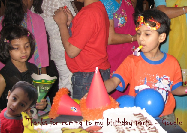 Kinder vor einem Tisch mit einem Kuchen, Luftballons und Partyhüten, mit weiteren Personen im Hintergrund.