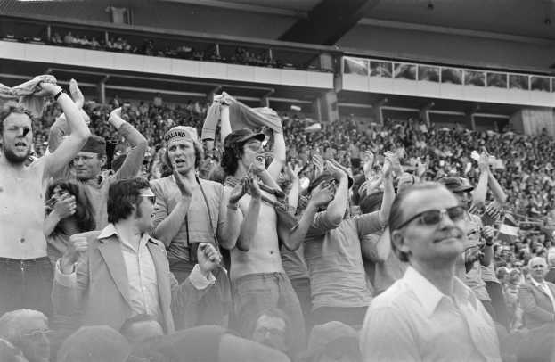 Schwarzes und weißes Foto einer vollen Tribüne mit Menschen, einige tragen Brillen.