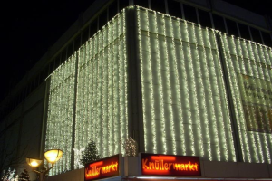 Ein festlich geschmücktes Gebäude in Berlin, Deutschland, mit Weihnachtslichtern umgeben von Bäumen und Laternenmasten, mit Texttafeln und einem sichtbaren Himmel im Hintergrund.