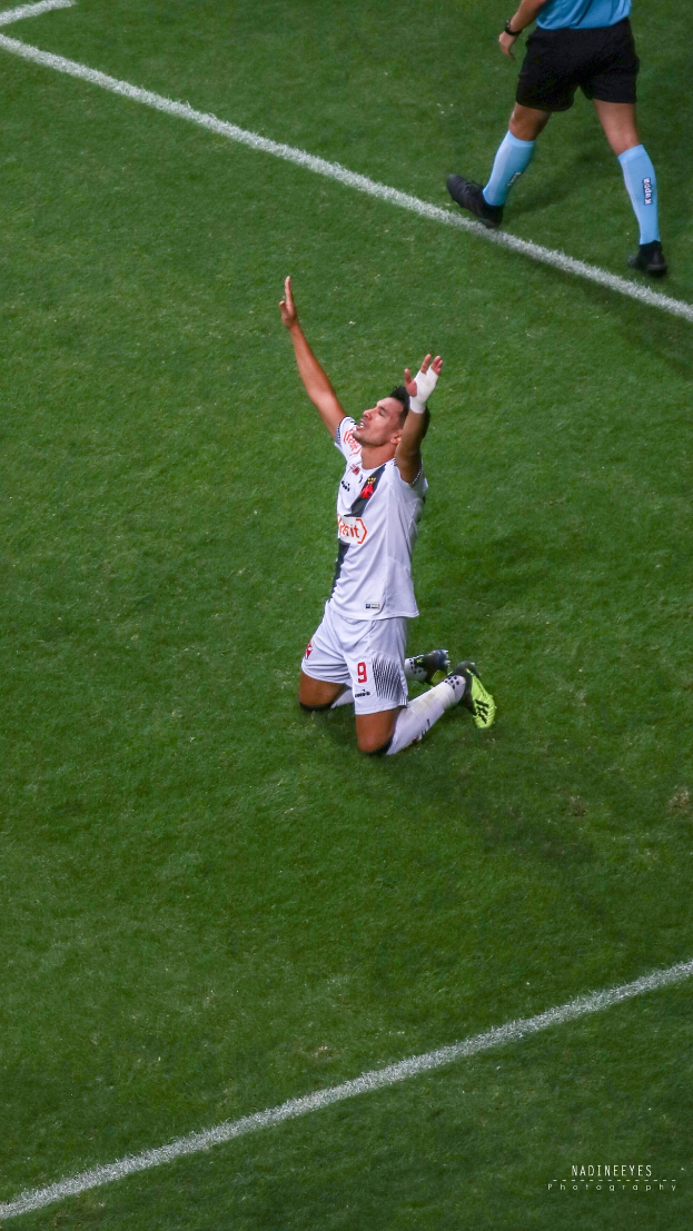Ein Fußballspieler kniet auf dem Boden mit ausgestreckten Armen in Feierlaune, trägt eine Sportuniform und -schuhe.