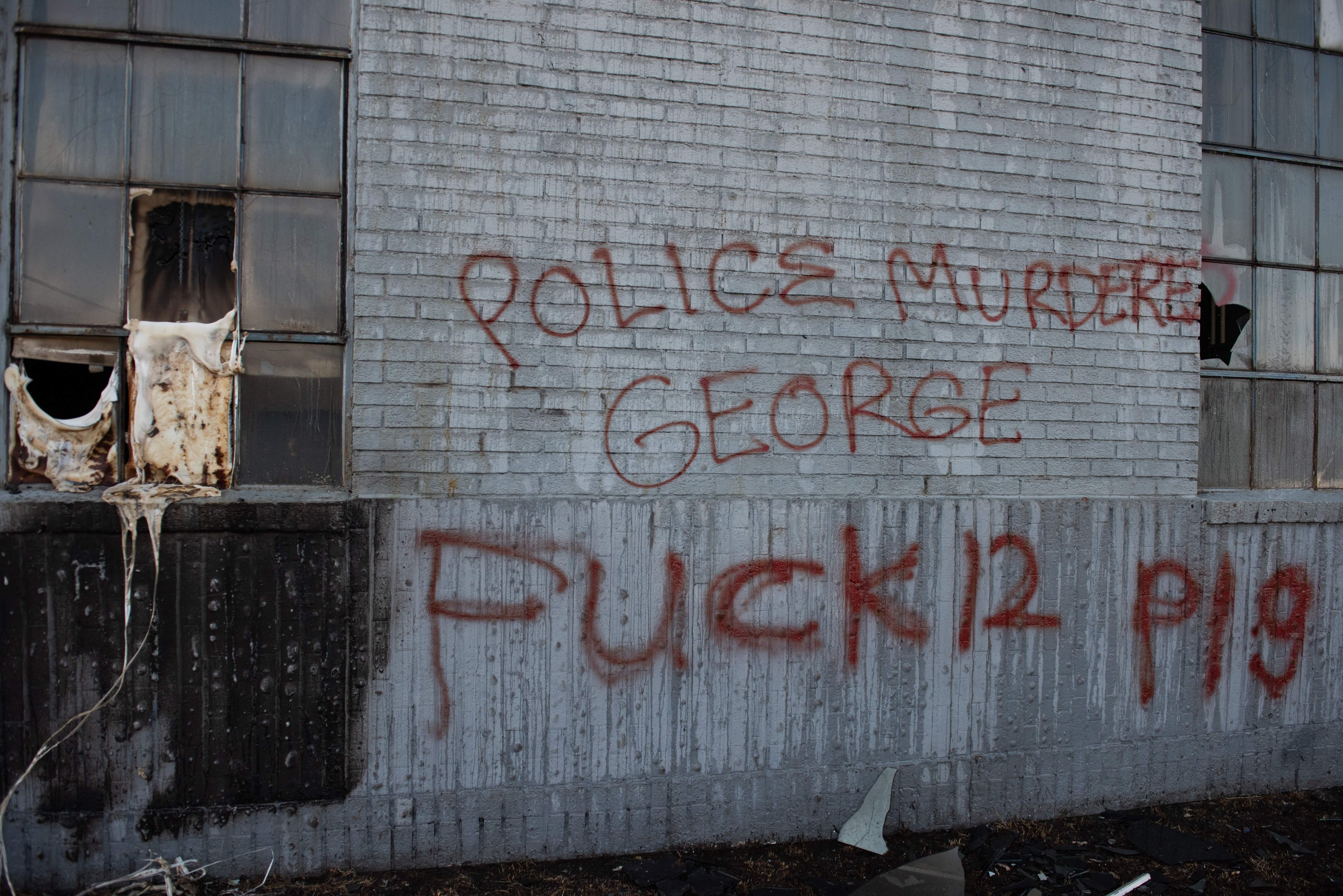 Graffiti auf einer Gebäudewand mit der Aufschrift "Polizei ermordet George Fuck 12 P19" und Fenstern und verstreuten Gegenständen davor.