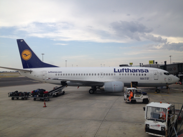 Lufthansa Airbus A320-200 auf dem Frankfurter Flughafen geparkt mit Bodenfahrzeugen, Verkehrskegeln und Beschilderung im Hintergrund unter einem bewölkten Himmel.