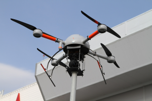 Eine Drohne ├╝ber einem Geb├Ąude mit einem Mast im Vordergrund und einem klaren blauen Himmel im Hintergrund.